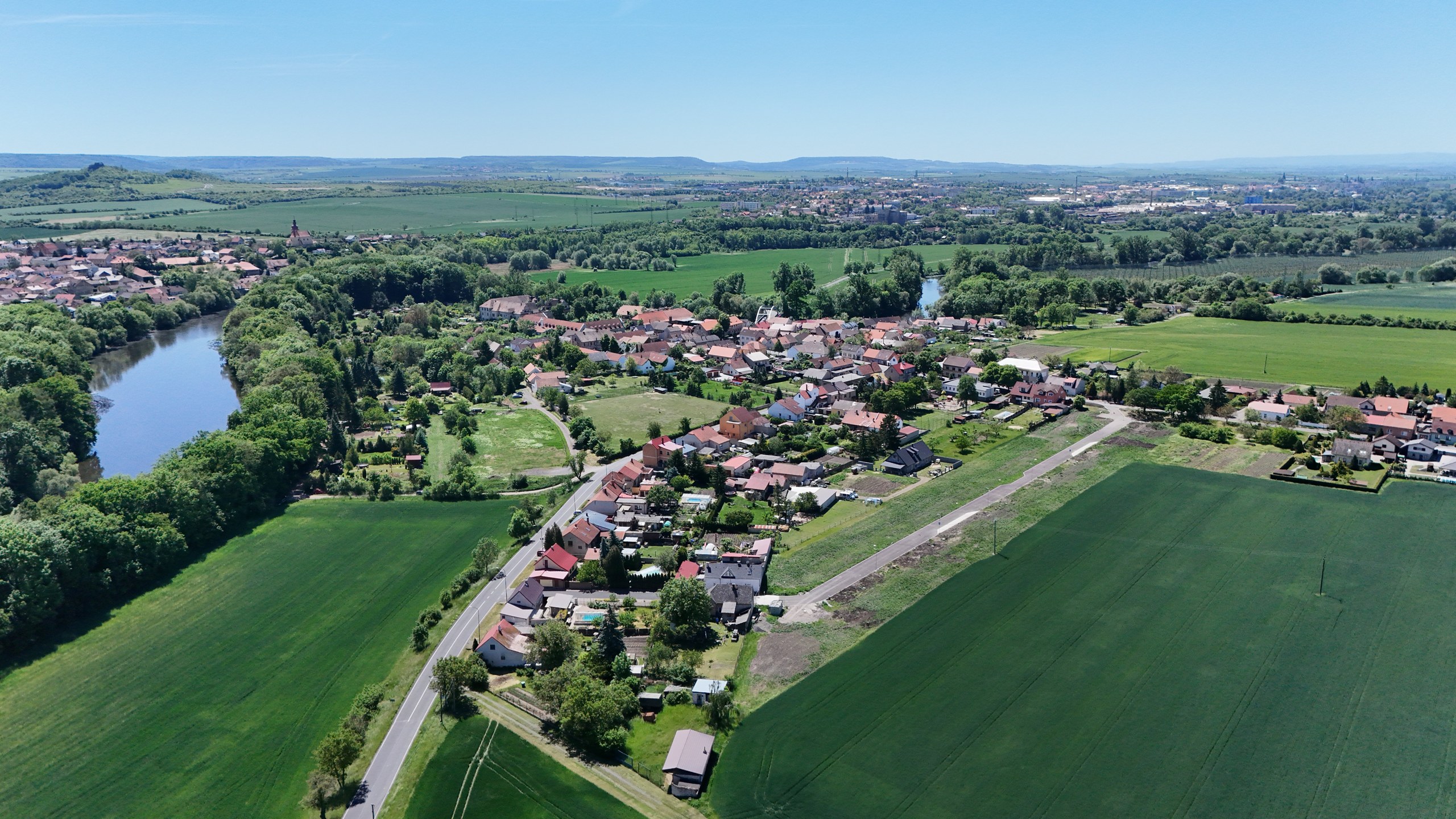 Pozemky u Tří dubů — krajina kolem obce, v pozadí kopce